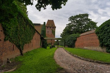 Ancient stone path leads to a historical tower surrounded by lush greenery and rustic walls in a...