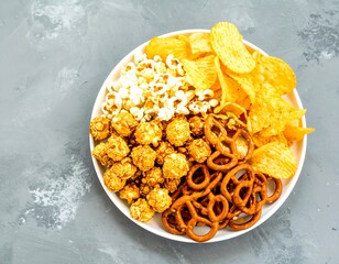 A plate overflowing with a variety of salty snacks, including popcorn, chips, and pretzels, creates a delightful visual feast.