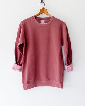 Cozy vintage-style maroon crimson red crewneck sweatshirt on wooden hanger, back view, minimalist fashion apparel mockup for branding, clothing design, boutique, or online shop display