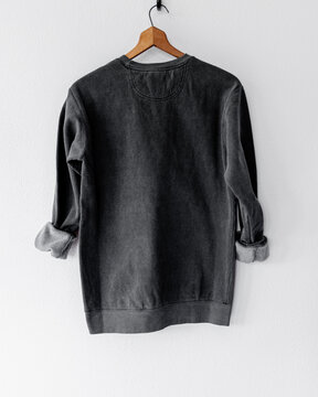 Cozy vintage-style dark gray charcoal black crewneck sweatshirt on wooden hanger, back view, minimalist fashion apparel mockup for branding, clothing design, boutique, or online shop display