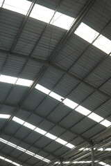 Industrial warehouse roof structure with metal beams and skylight panels allowing natural light inside. A detailed architectural view highlighting strength, and industrial construction design