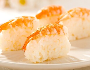 Close-up of three shrimp nigiri sushi pieces on a white plate, showcasing the delicate presentation of the cooked shrimp atop fluffy rice.