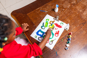 Little African girl engaged in creative art painting activity at home.