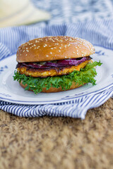 Homemade veggie burger with lettuce, red cabbage, and sesame seed bun served on a white plate. healthy plant-based burger with colorful layers and rustic food styling for casual dining or picnic theme