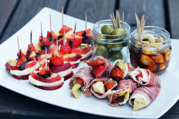 Assorted antipasto platter featuring prosciutto rolls filled with artichokes and sun-dried tomatoes, alongside jars of marinated mozzarella and olives. Perfect for illustrating festive entertaining
