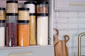 Organized kitchen pantry with cylindrical plastic jar for storing loose products,  in grey tones
