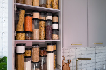 Organized kitchen pantry with cylindrical plastic jar for storing loose products,  in grey tones