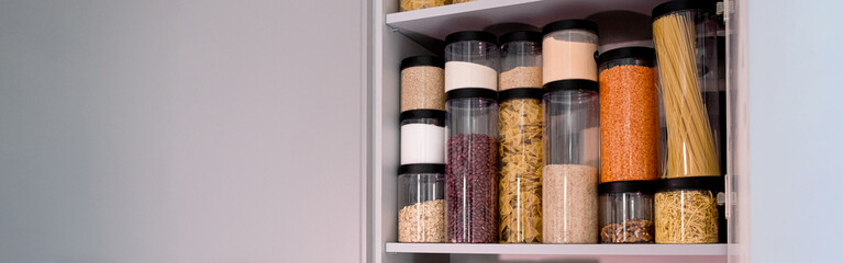 Organized kitchen pantry with cylindrical plastic jar for storing loose products,  in grey tones. banner