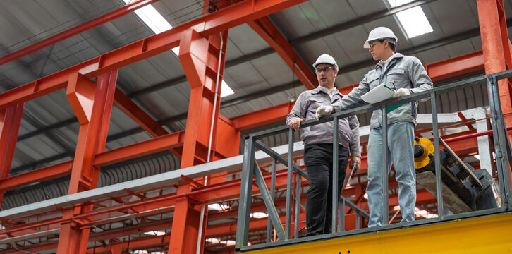 Engineers inspecting equipment and discussing maintenance procedures inside a modern industrial factory. Safety, teamwork, and production quality control in a manufacturing plant.