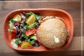 Delicious gourmet burger served with fresh garden salad on wooden table