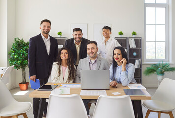Group portrait of six multiethnic, Caucasian and African business people, executives or marketing department members gathered in office with laptop, looking at camera. Career, professionalism, unity
