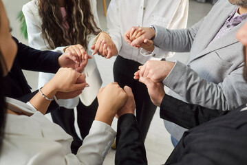 Close-up of group of diverse businesspeople dressed in formal wear stands in circle, holding their hands in symbolic gesture of unity, trust and support. Concept of synergy, teamwork and solidarity