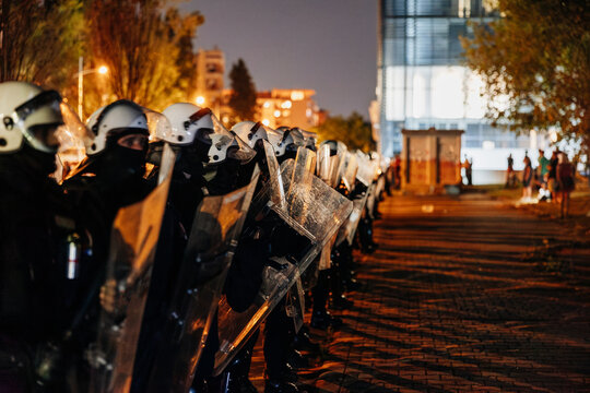 Law enforcement officers in riot gear standing firm during nighttime protest in urban area