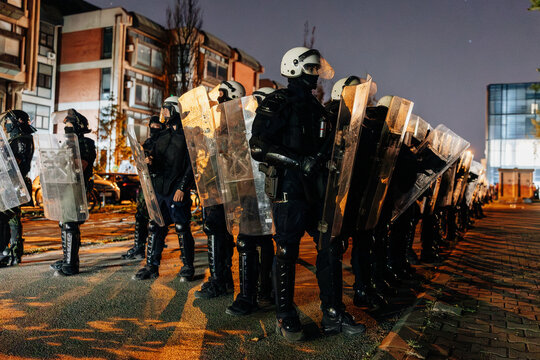 Riot police stand ready during a nighttime protest in an urban area amid tensions and unrest
