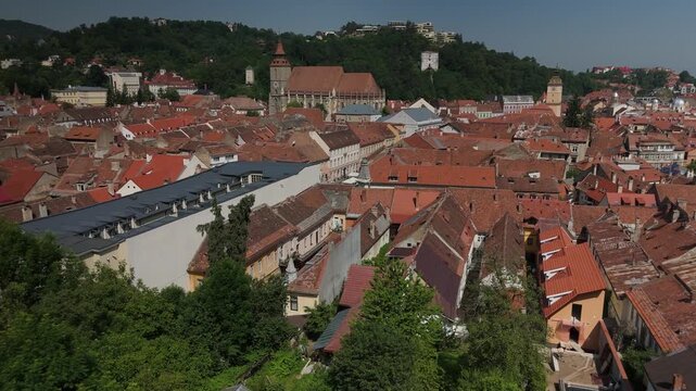 Ascending drone flight over Brasov old town from medieval tower, revealing Piata Sfatului, Casa Sfatului, Biserica Neagra and Turnul Alb on a bright summer morning