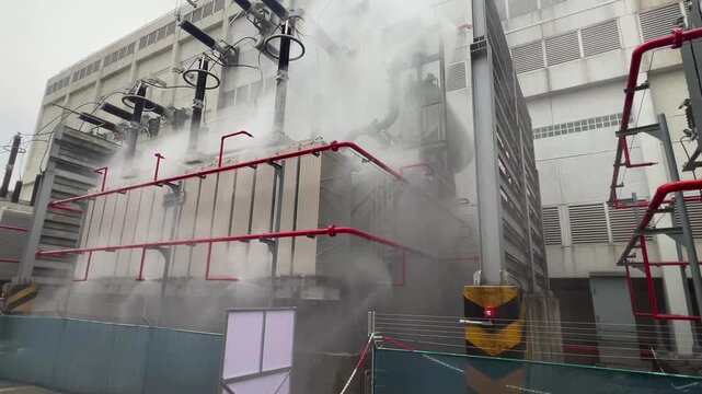 Transformer fire protection power substation with grey smoke rising, red pipe system, safety response active industrial emergency drill shows smoke, foam, water mist, sprinkler hazard control power