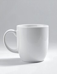 Obraz premium A simple, clean white mug is displayed against a neutral backdrop, showcasing its smooth, polished surface and sturdy handle.