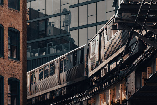 Curving elevated train passes historic brick facades and reflective glass towers, showcasing urban transit, architectural contrast and moody evening light.