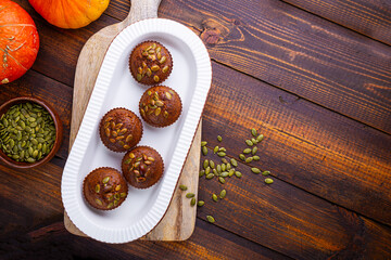 Autumn pumpkin cupcakes or baked muffins with fresh pumpkin and pumpkin seeds for Thanksgiving day on dark wooden background. Top view, copy space for text