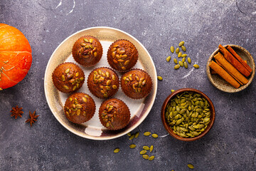 Autumn pumpkin cupcakes or baked muffins with fresh pumpkin and pumpkin seeds for Thanksgiving day on grey background. Top view