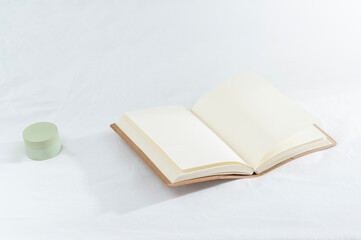Open Notebook Resting on a White Surface With a Small Green Container Beside It