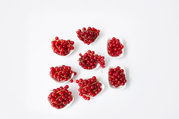 Minimalistic composition of fresh red currant berries arranged in small white bowls on a clean white background. Top view with vibrant color contrast.