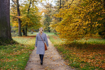 Fashion woman in houndstooth coat walking on path through autumn park