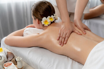 Naklejka premium Caucasian couple customer enjoying relaxing anti-stress spa massage and pampering with beauty skin recreation leisure in day light ambient salon spa at luxury resort or hotel. Quiescent