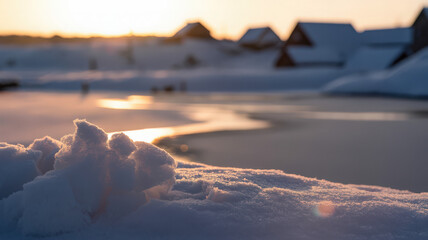Snowy landscape with frozen lake and distant buildings at sunset creating a peaceful winter scene