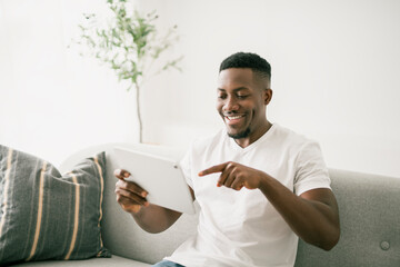 Black men wearing white shirt on sofa holding tablet