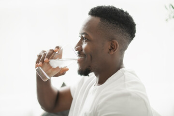 Black men wearing white shirt on sofa at home drink water