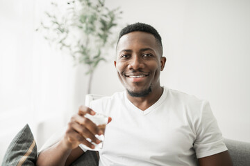 Black men wearing white shirt on sofa at home drink water