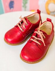 Two vibrant red leather children's shoes with light pink shoelaces sit on a white surface, showcasing a delightful color combination.