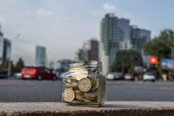 Glass jar with 100 Kazakhstani tenge banknotes against the backdrop of a city center avenue with high-rise buildings