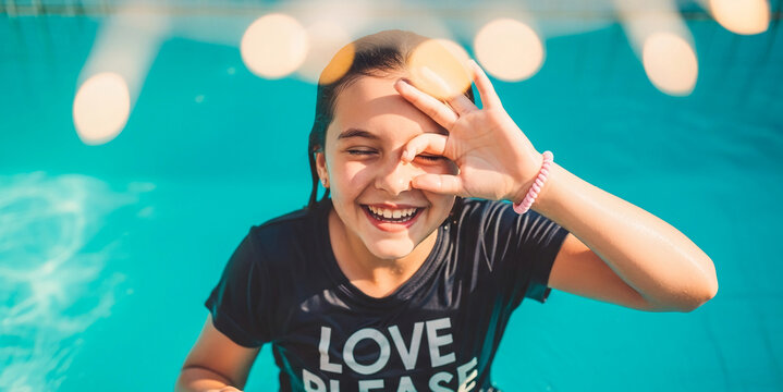 Smiling girl in swimming pool, making ok sign with hand, turquoise water background, summer fun, joyful expression - Powered by Adobe