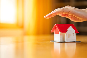 Protecting Your Home A Hand Gently Covers a Miniature House on a Wooden Surface, Symbolizing Safety, Security, and the Importance of Homeownership and Insurance Coverage