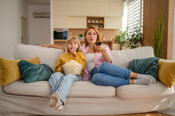 Obraz premium Mother and daughter watching television and eating popcorn on sofa