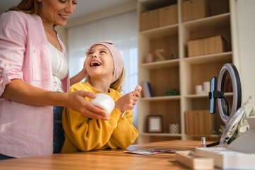 Mother helping daughter applying cream on face at home
