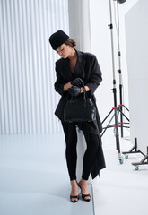Girl model in stylish clothes with bag posing in studio