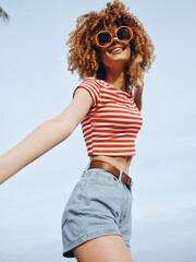 A young woman with curly hair wears a red striped crop top and denim shorts, posing cheerfully...