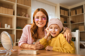 Mother and daughter applying cosmetic patches under eyes at home