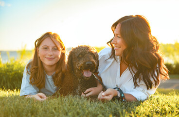 brown portuguese water dog outdoors on grass with mother and daughter