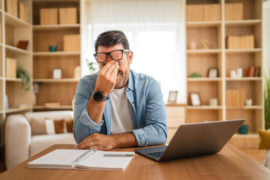 Tired businessman rubbing eyes while working from home
