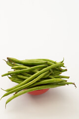 Closeup of fresh green beans stacked in red bowl, isolated on white.