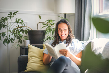 woman sitting and reading book on a sofa at home