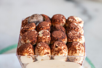 A rich and creamy tiramisu sits elegantly in a clear container, topped with cocoa-dusted swirls of mascarpone.