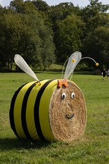 Cute bee sculpture made from a round hay bale, decorated with black stripes, googly eyes, and wings. Perfect for autumn garden decoration, festivals, or farm-themed events © Nadiia