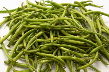 Fresh green beans spread out on a white background, showing their natural texture and color.