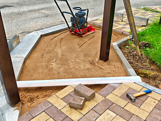 Construction of a patio base with compacted sand and paving bricks in a residential area during daylight
