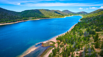 Fototapeta premium Aerial Pristine Lake Surrounded by Forest and Mountains in Summer Sunlight
